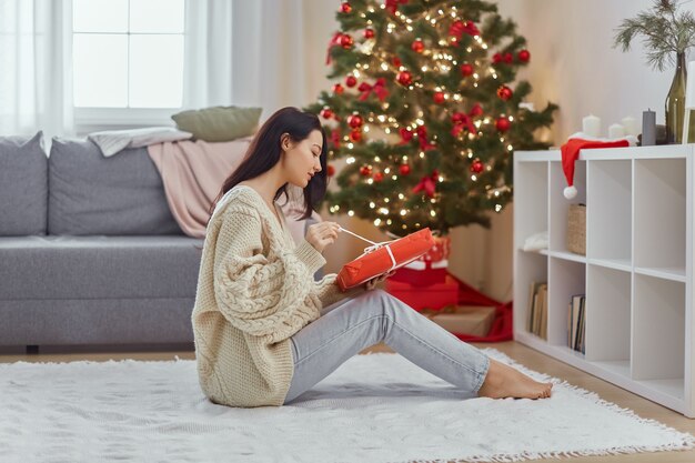 Donna con regalo nella confezione regalo vicino all'albero di natale a casa