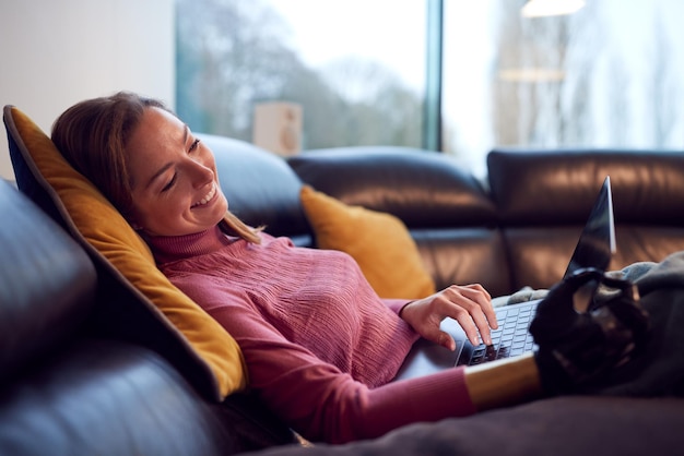 Woman With Prosthetic Arm Using Laptop Relaxing On Sofa At Home