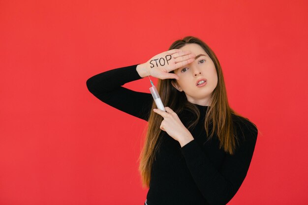 Woman with protective mask hold medical syringe in hand on red background Stop drugs