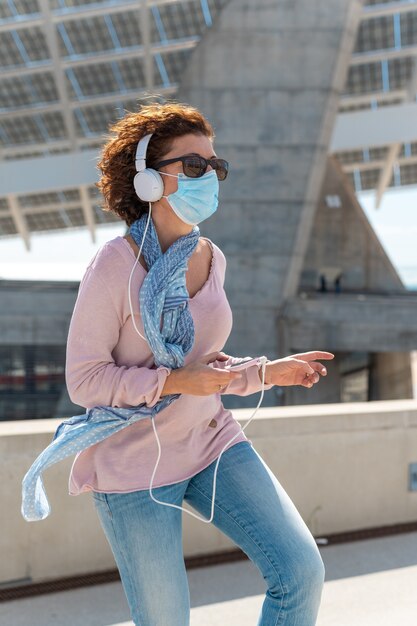 Donna con maschera protettiva e occhiali da sole ascoltando musica e balli