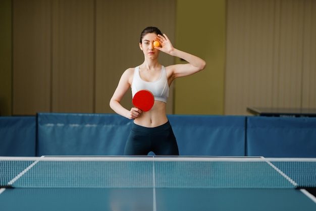 Woman with racket shows ping pong ball indoors