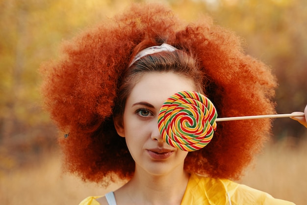 Woman with red afro in a yellow raincoat with big Lollipop