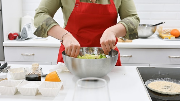 Donna con il grembiule rosso che cucina in una cucina bianca