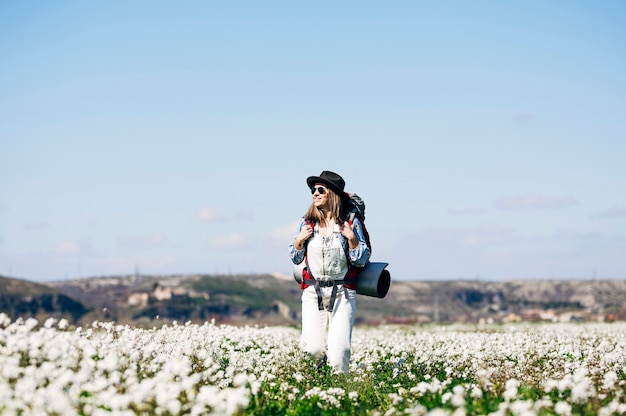 Photo woman with red backpack and hat walking through flowery field