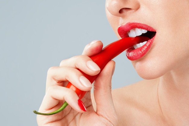 Woman with a red chili pepper between her teeth