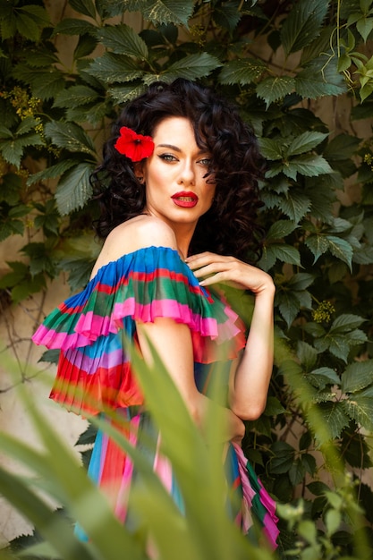 A woman with a red flower in her hair stands in front of a green wall.