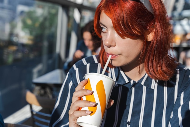 a woman with red hair drinking from a cup with a straw in it