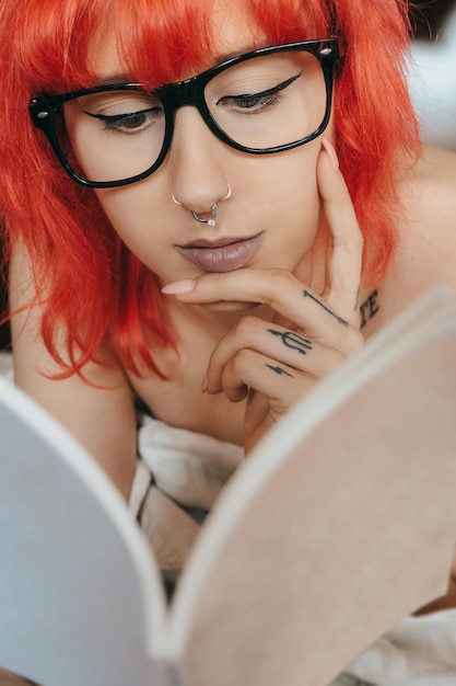 Woman with red hair and a nose piercing reading a book