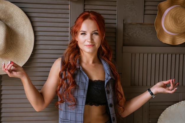 A woman with red hair poses against a wall with her arms outstretched