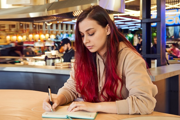 woman with red hair sitting in a cafe and writes in a diary