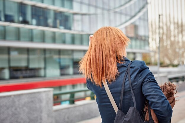 A woman with red hair walks in front of a building