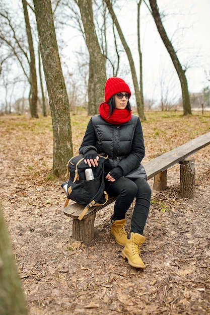 Woman with red hat in black jacket, backpacker traveler sitting on bench, relaxing