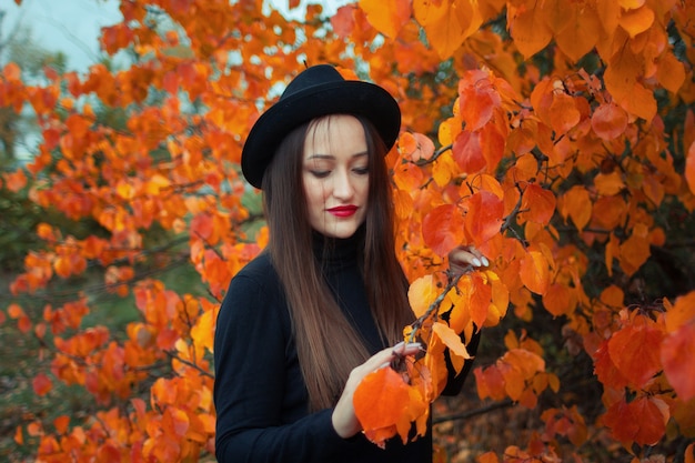 woman with red lipstick in a hat over an autumn tree