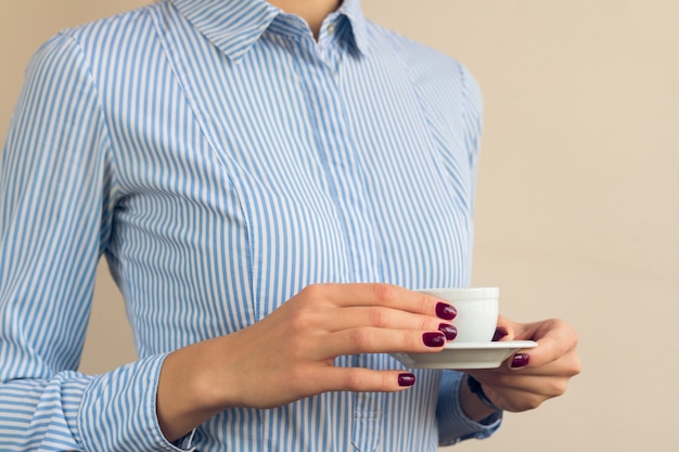 Woman with red manicure and blue shirt holding a Cup of coffee close up