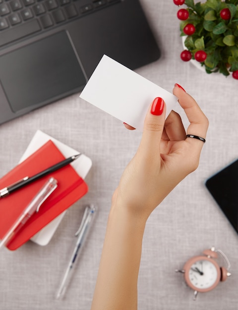 Woman with red manicure holding blank business card on gray table