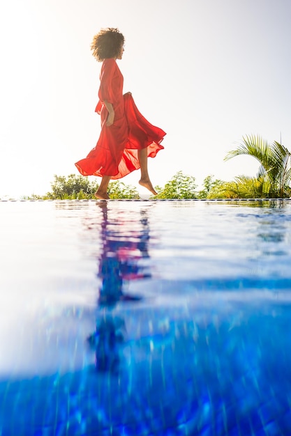 Woman with red summer dress posing next to a pool