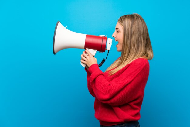 Woman with red sweater over blue wall shouting through a megaphone