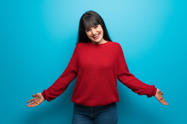 Woman with red sweater over blue wall smiling