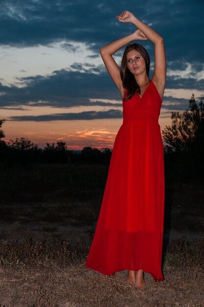 Foto donna con ombrello rosso in piedi sul campo contro il cielo durante il tramonto