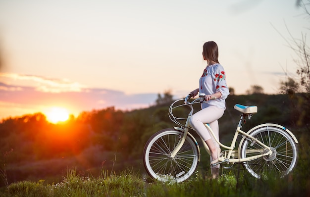 夕方の丘の上にレトロな自転車を持つ女性