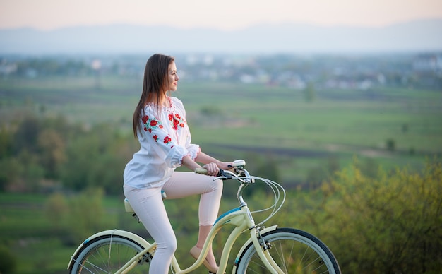 夕方の丘の上にレトロな自転車を持つ女性