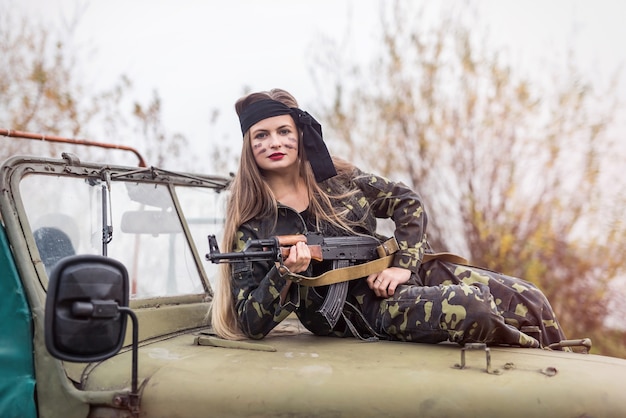 Woman with rifle posing on military car