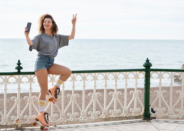 Woman with roller skates taking a selfie and sitting on a fence outdoors