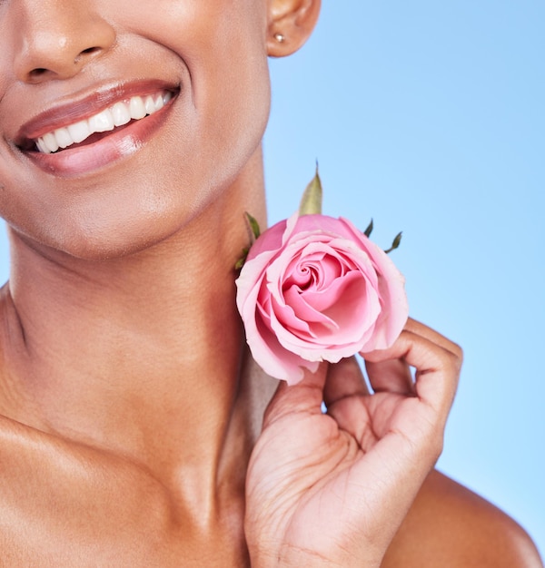 Woman with rose closeup and natural beauty with sustainable skincare isolated on blue background Wellness skin glow and eco friendly cosmetics with pink flower product and nature in a studio