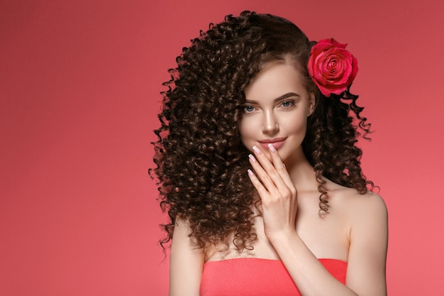 Woman with rose flower. Beauty female portrait with beautiful rose flower and salon hairstyle over pink manicure nails  background. Studio shot.