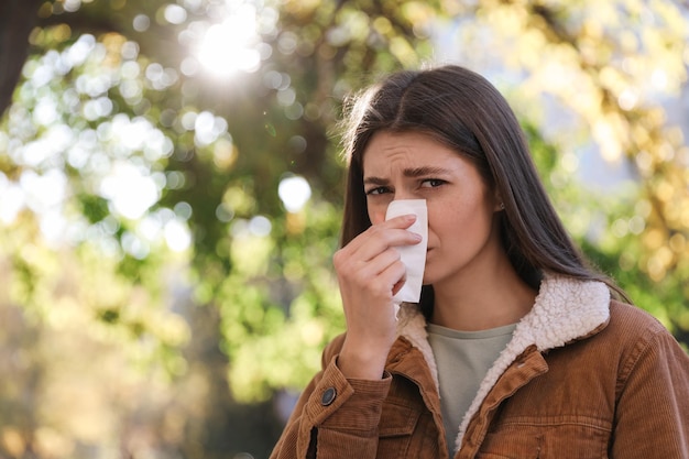 Woman with runny nose in park space for text