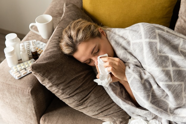 Foto donna con un sintomo di naso che cola sdraiata sotto la coperta a casa