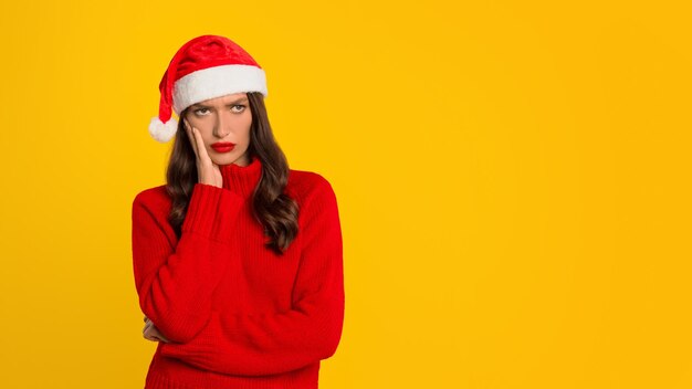 Woman with santa hat poses with displeased expression yellow backdrop