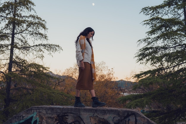 Woman with a scarf walk in an autumn park at sunset with the moon in the background