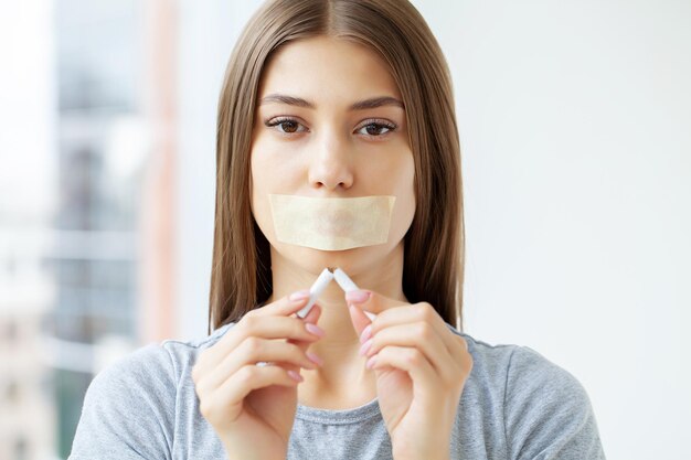 Woman with a sealed mouth holding a broken cigarette