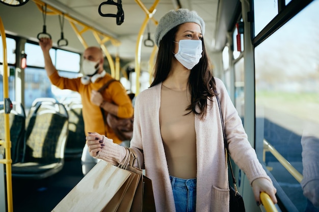 Donna con borse della spesa che indossano una maschera facciale mentre si sposta in autobus