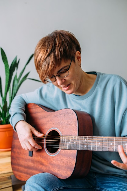 woman with short hair enjoys playing guitar at home music lessons for adults