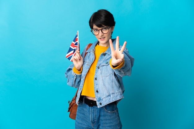 Woman with short hair holding an United Kingdom flag isolated on blue background happy and counting three with fingers