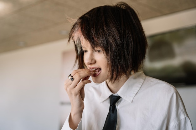 Woman with short hair putting food in her mouth with her hand, blurred horizontal background