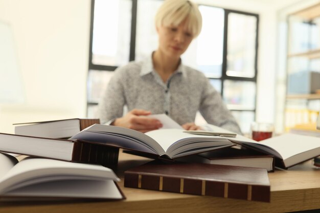 Una donna con i capelli corti cerca informazioni in grossi libri per un lavoro da laureato seduta a un tavolo