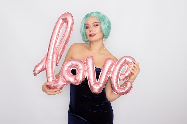 Woman with short mint hair in dark blue velvet dress holding balloon with word LOVE