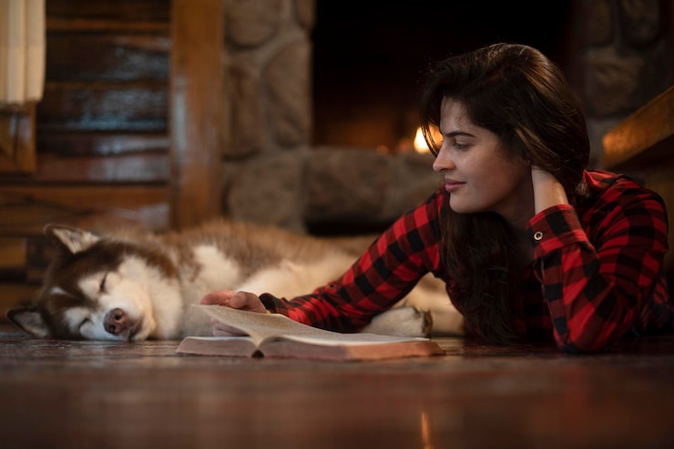 Photo woman with siberian husky dog sitting on the wooden floor in front of the burning fireplace
