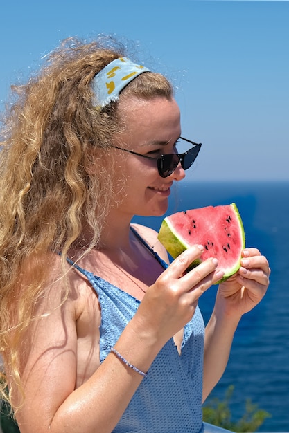 woman with a slice of watermelon in swimsuit looking at sea view