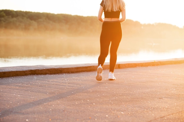Женщина со стройной мускулистой фигурой бегает в черной спортивной одежде и белых кроссовках