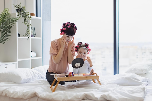 Photo woman with small child looking in mirror and applying moisturizing face masks