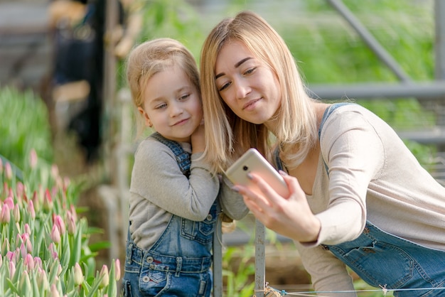 A woman with a small daughter take a selfie in a greenhouse with flowers in spring.