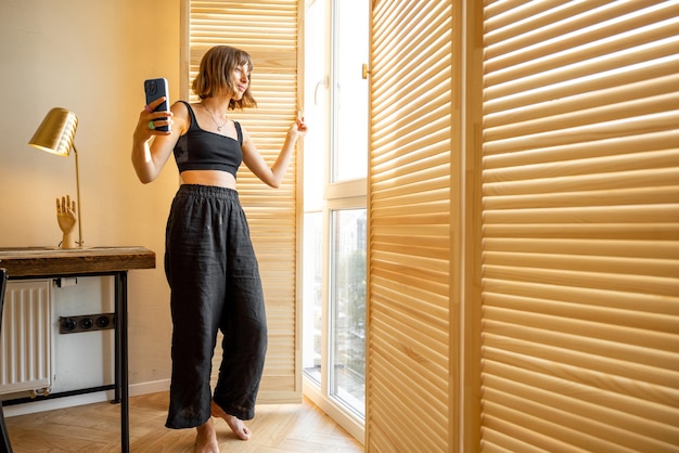 Woman with smart phone near window at home