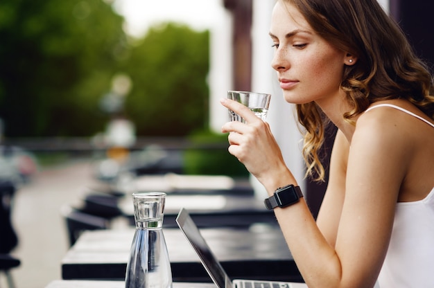 写真 夏のカフェで水を飲むスマートウォッチを持つ女性