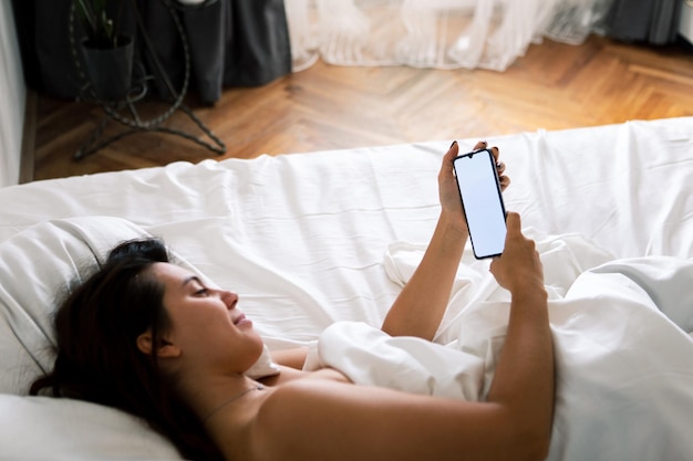 Woman with smartphone in bed with white sheets