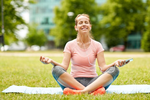 woman with smartphone and hones meditating at park