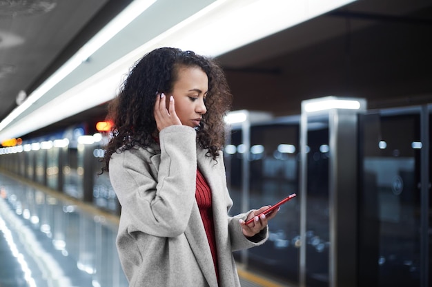 Donna con uno smartphone che digita sms in piedi sulla piattaforma della metropolitana